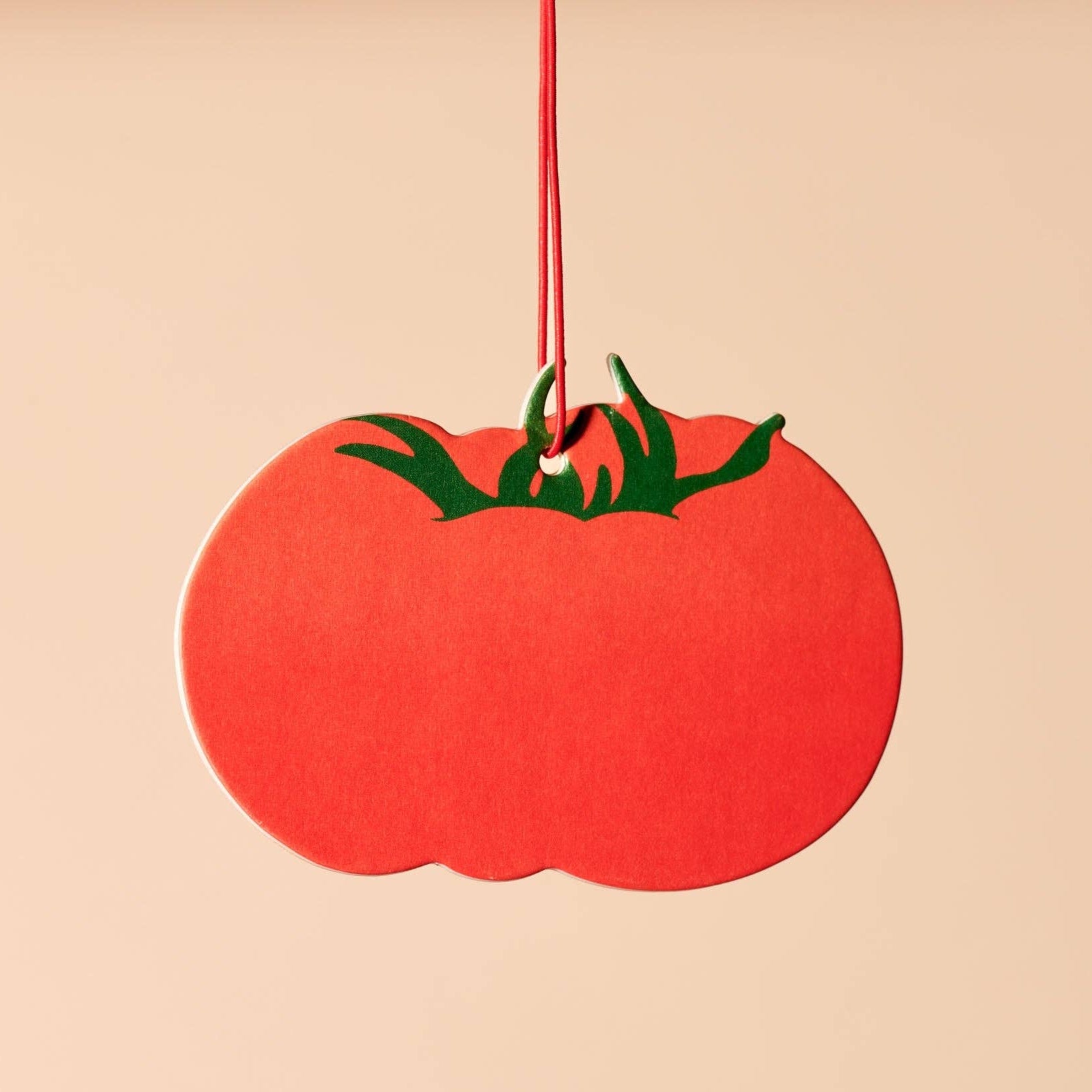 Red tomato-shaped air freshener with green stem and red string on a beige background