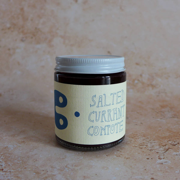 Jar of salted currant comote on a textured beige surface