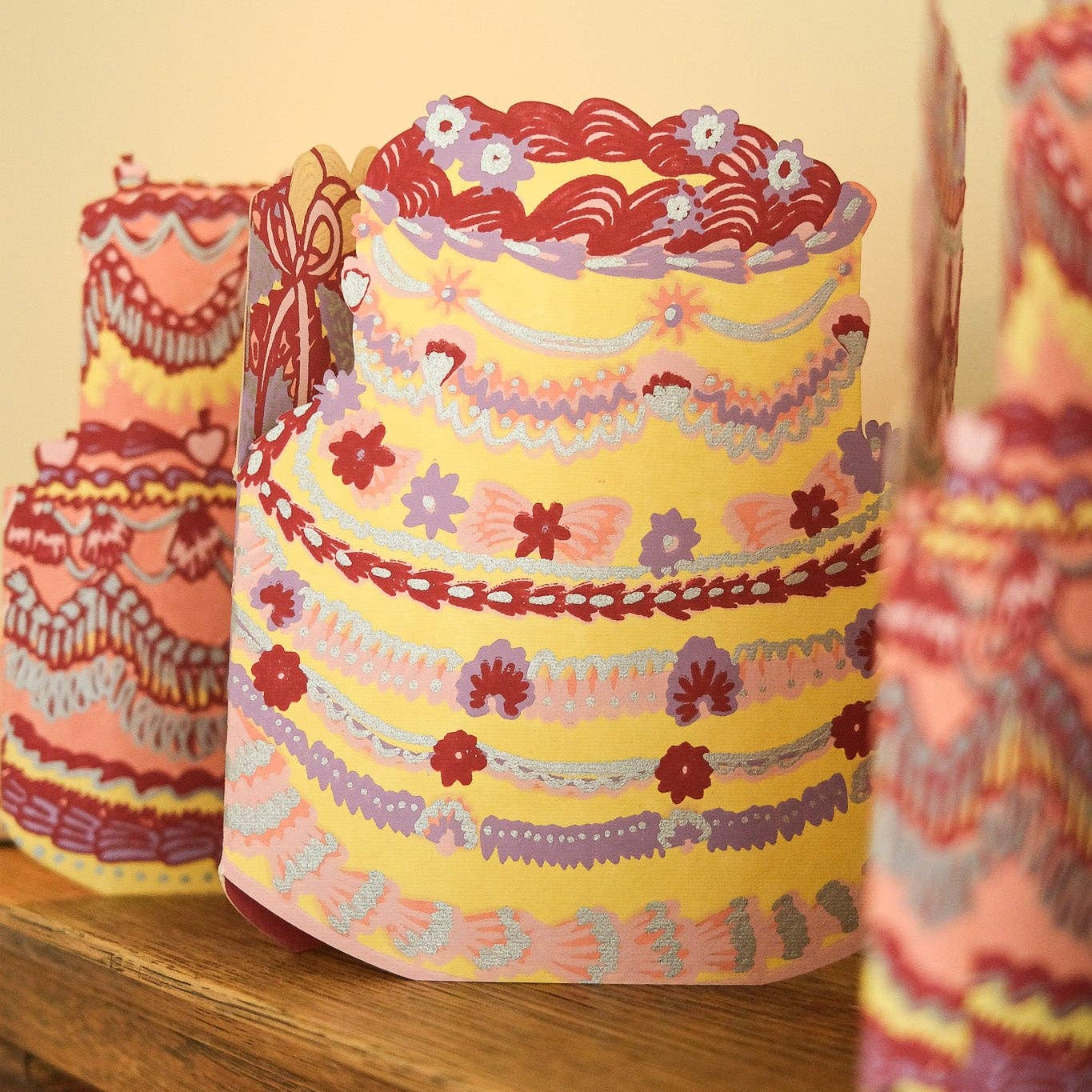 Decorative paper cake models on a wooden surface with a plain background
