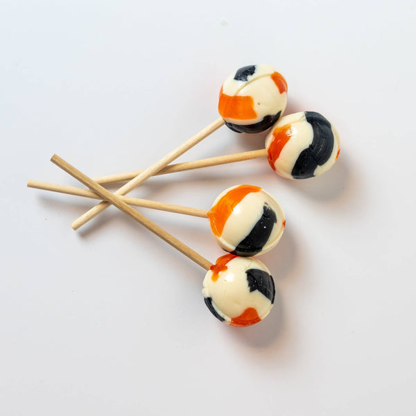 Four marbled lollipop treats with orange, black, and off-white swirls on wooden sticks, arranged on a clean white background.