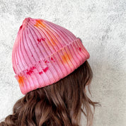 Pink knit beanie with gradient effect worn by a person against a light gray background