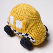 A hand-knit yellow toy car with white window details, black wheels, and a black-and-white striped front bumper, photographed on a light neutral background.