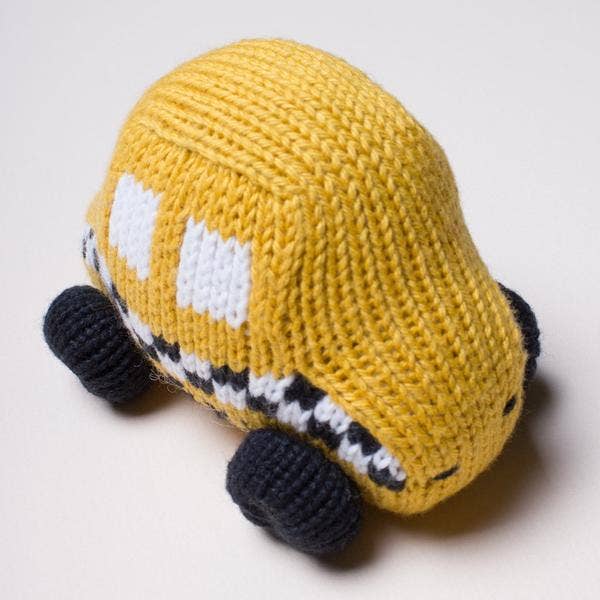 A hand-knit yellow toy car with white window details, black wheels, and a black-and-white striped front bumper, photographed on a light neutral background.