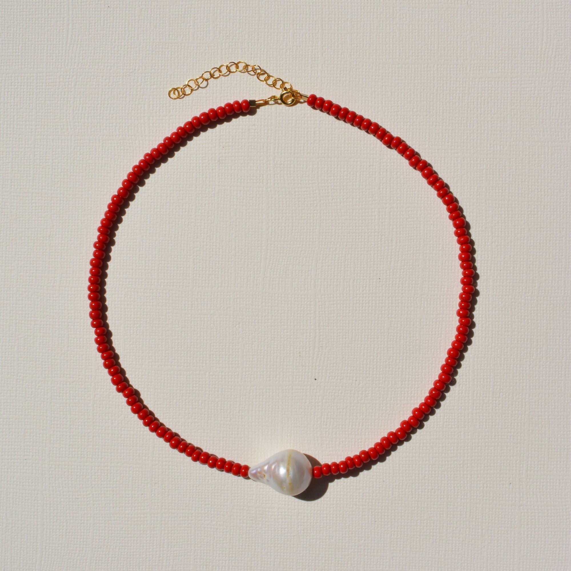 Red beaded necklace with a pearl pendant on a light gray background