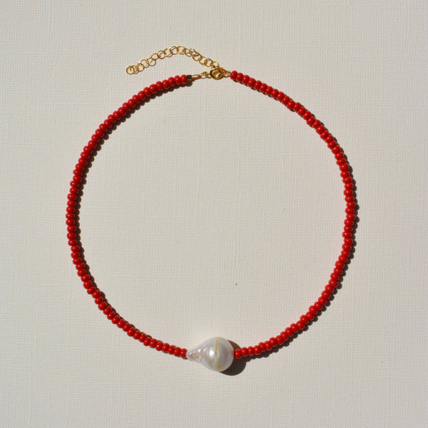 Red beaded necklace with a pearl pendant on a light gray background