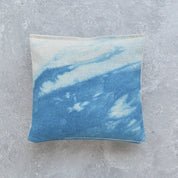 A square lavender sachet featuring a blue and white tie-dye or watercolor pattern, displayed on a textured gray concrete surface.