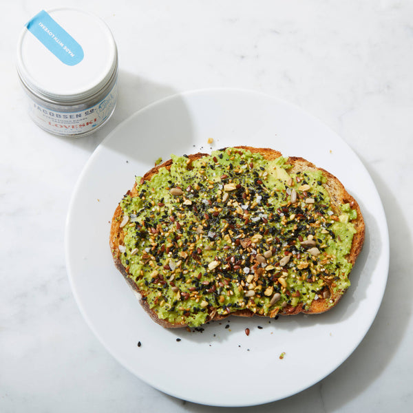 Avocado toast on a white plate with a jar with a white top in the background.