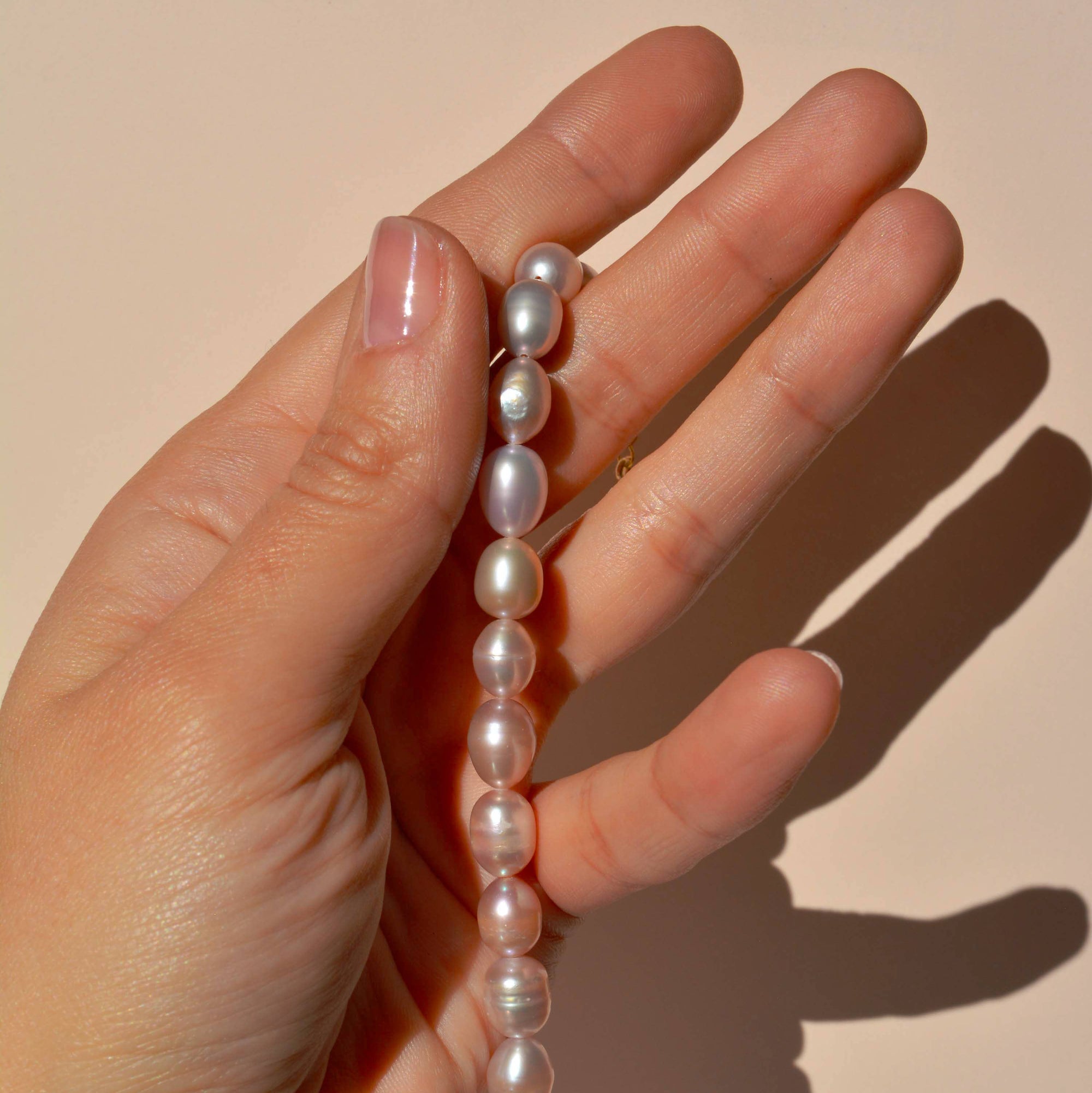 Hand holding a pearl bracelet against a plain background