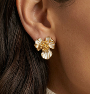 Close-up of a gold and white floral earring on an ear.