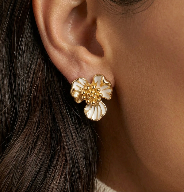 Close-up of a gold and white floral earring on an ear.