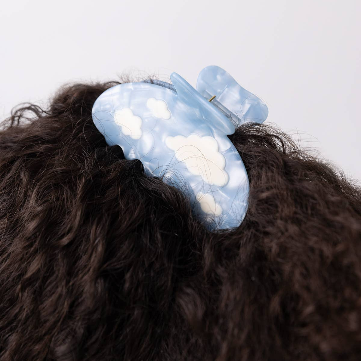 Blue hair clip with cloud design on a person's hair against a white background