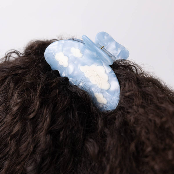 Blue hair clip with cloud design on a person's hair against a white background