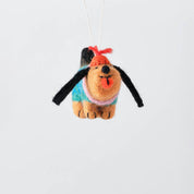 A handcrafted felt dog ornament hanging from a white string against a clean, light gray background. The dog features tan fur, black floppy ears, a turquoise sweater, a pink collar, and a red bow on its head.