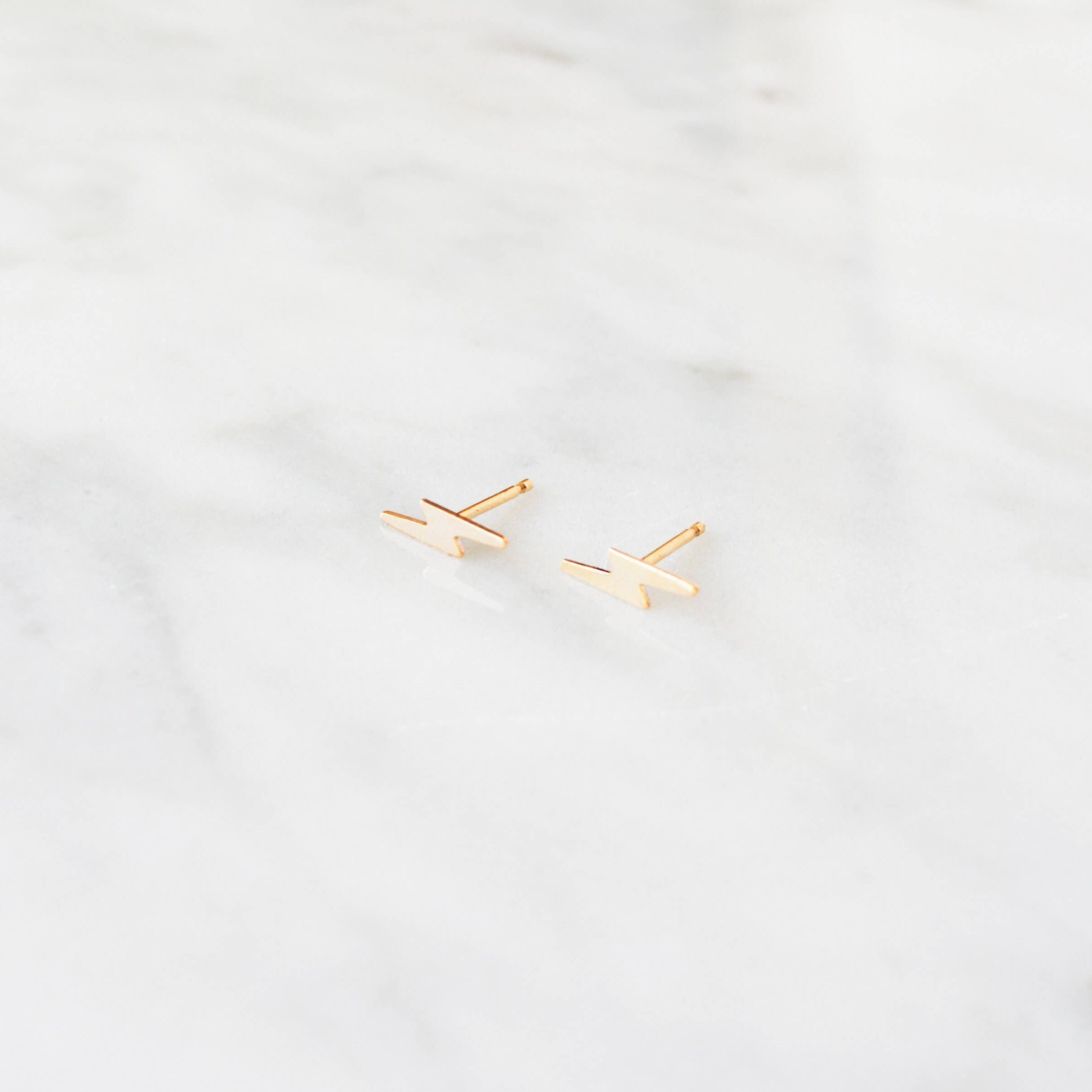 Gold lightning bolt shaped earrings on a light gray background