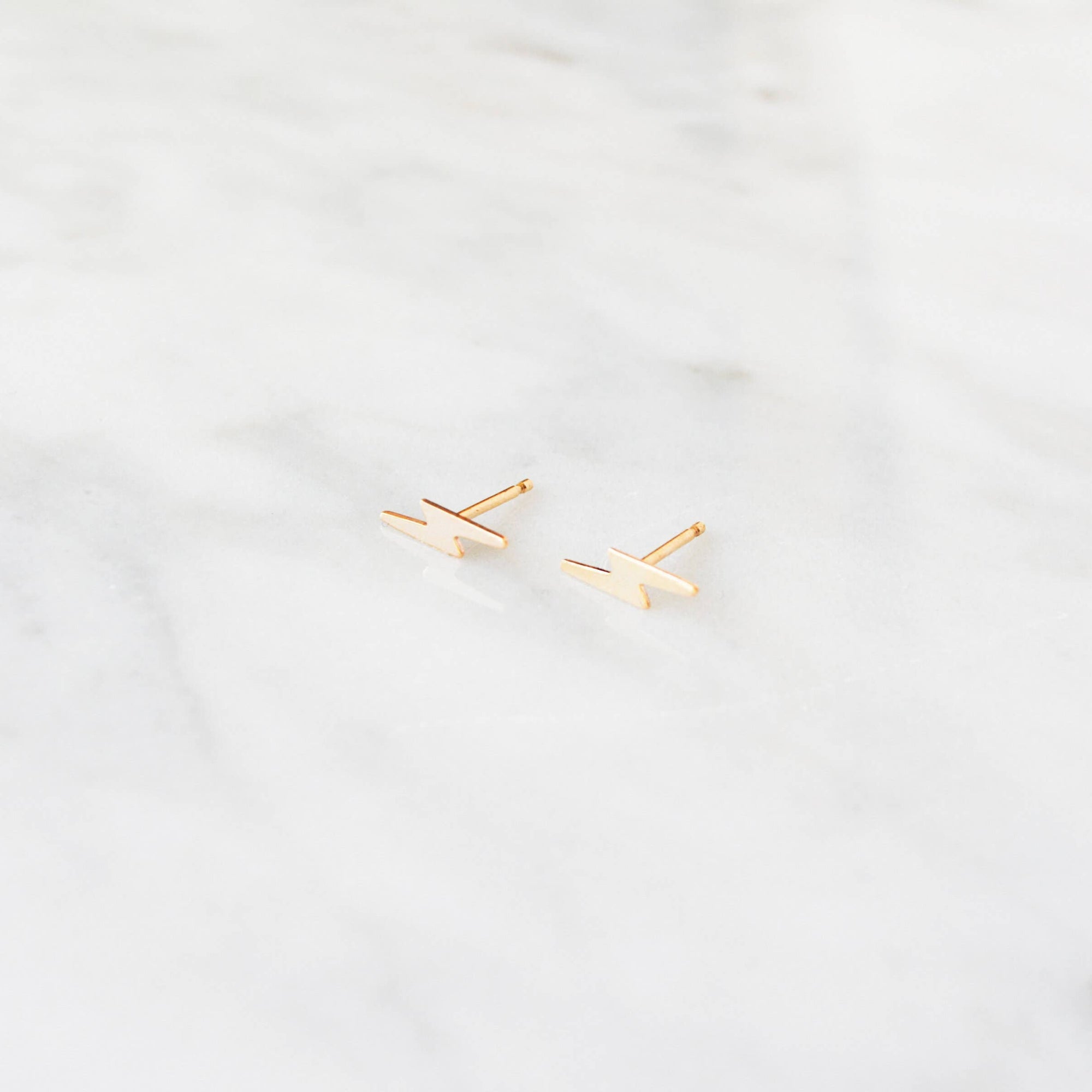 Gold lightning bolt shaped earrings on a light gray background