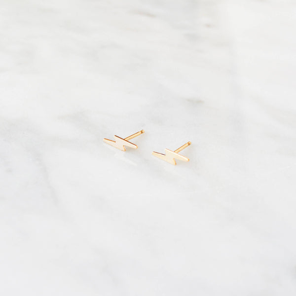 Gold lightning bolt shaped earrings on a light gray background