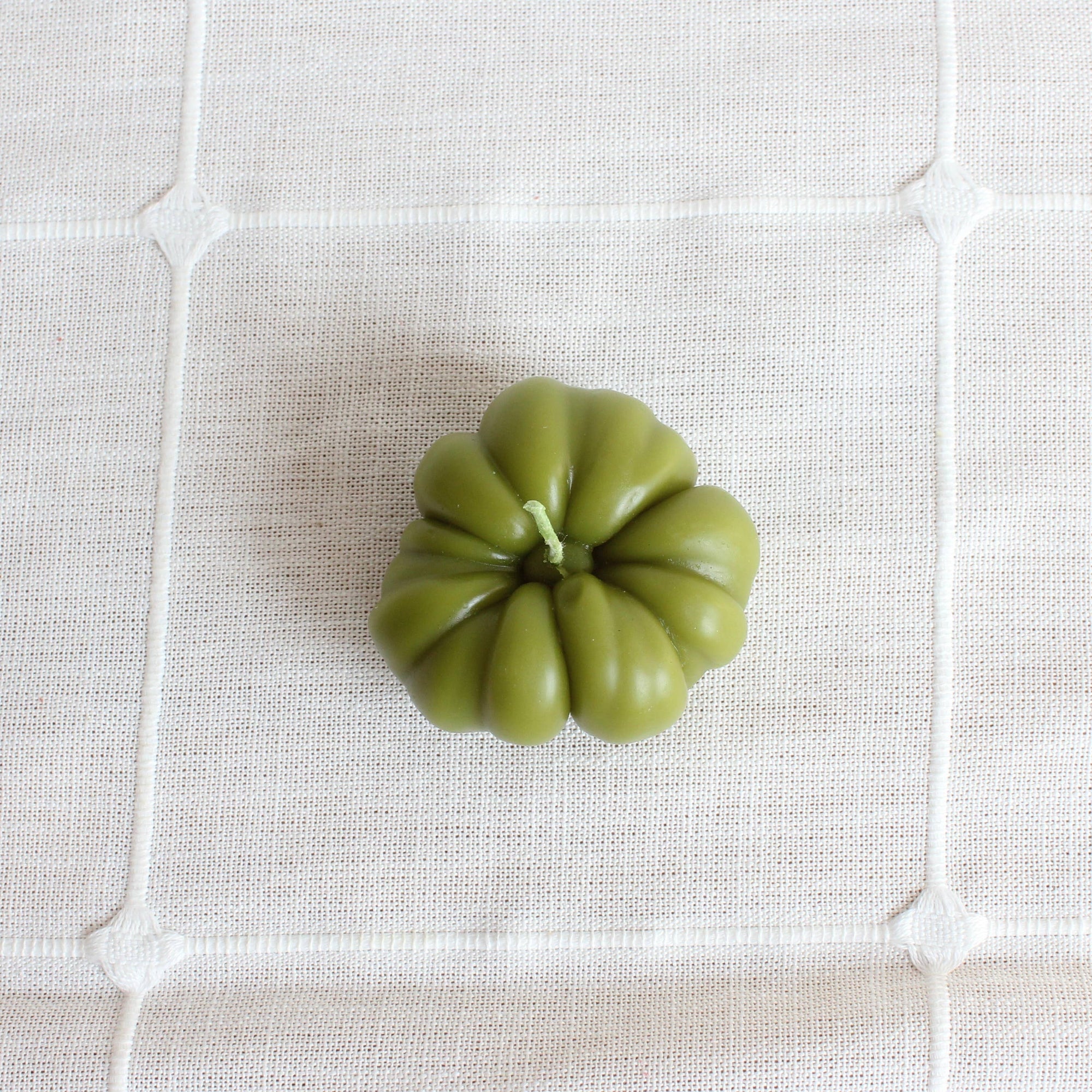 Green candle shaped like a heirloom tomato on a textured white surface