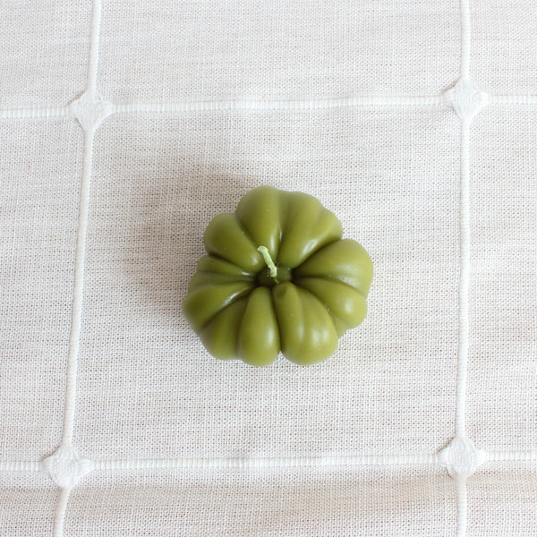 Green candle shaped like a heirloom tomato on a textured white surface