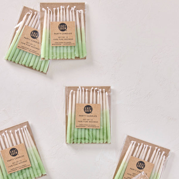 Set of green and white candles in brown paper packaging on a light gray background
