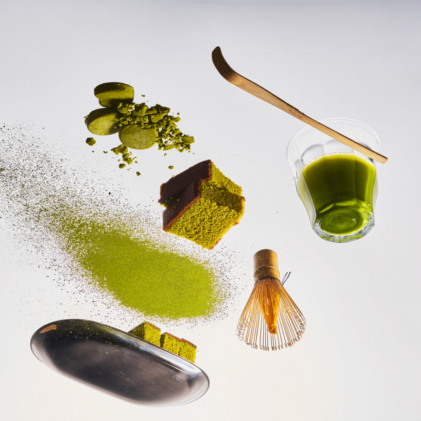 Matcha green tea preparation set with powder, leaf, whisk, and glass on a white background