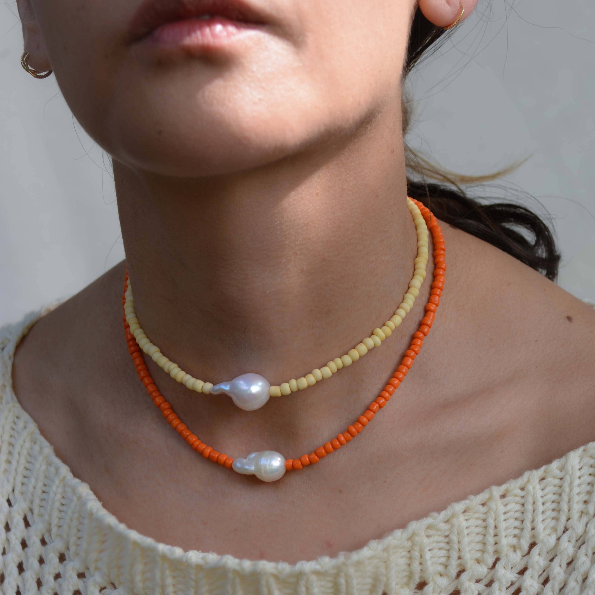 Close-up of a person wearing two pearl necklaces on an off-shoulder white top.