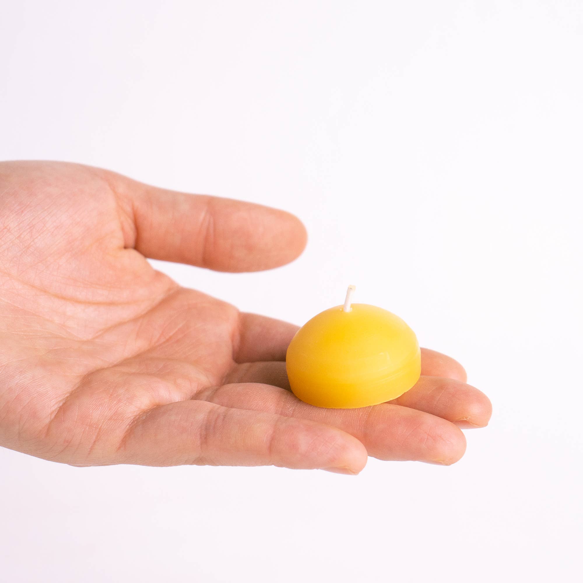 Hand holding a small yellow candle against a white background