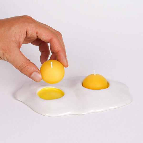 Hand placing a yellow candle into a white ceramic dish shaped like an egg.