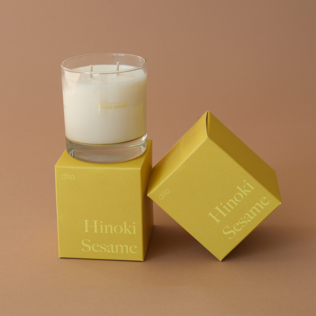 Hinoki Sesame Candle by dilo, showcasing a warm glow in a minimalist glass container with natural wood accents.