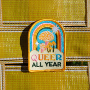 Embroidered patch with rainbow design and 'Queer All Year' text on a textured yellow background