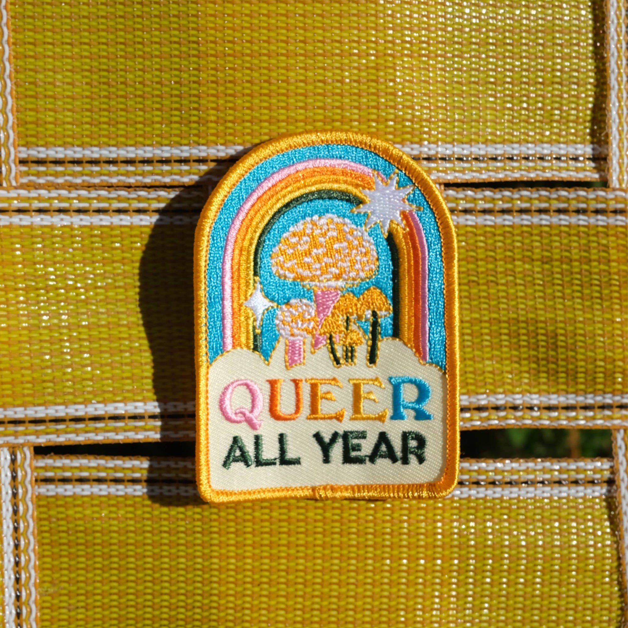Embroidered patch with rainbow design and 'Queer All Year' text on a textured yellow background