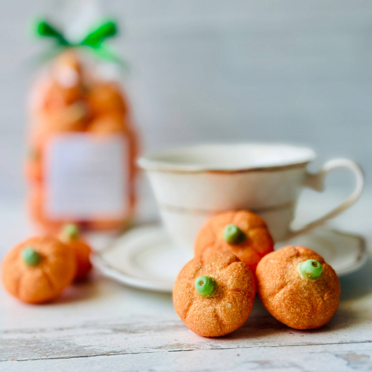 A teacup on a wooden table with a small group of pumpkin shaped marshmallows at the forefront.
