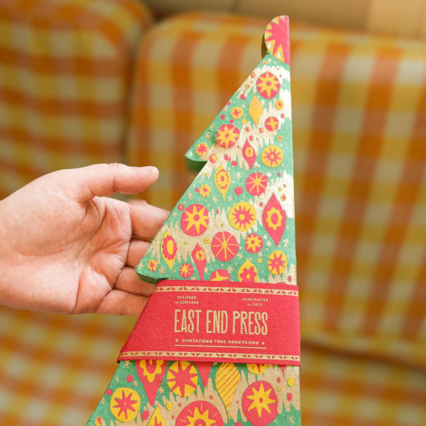 Colorful Christmas tree-shaped product with 'East End Press' branding held by a hand against a checkered background.