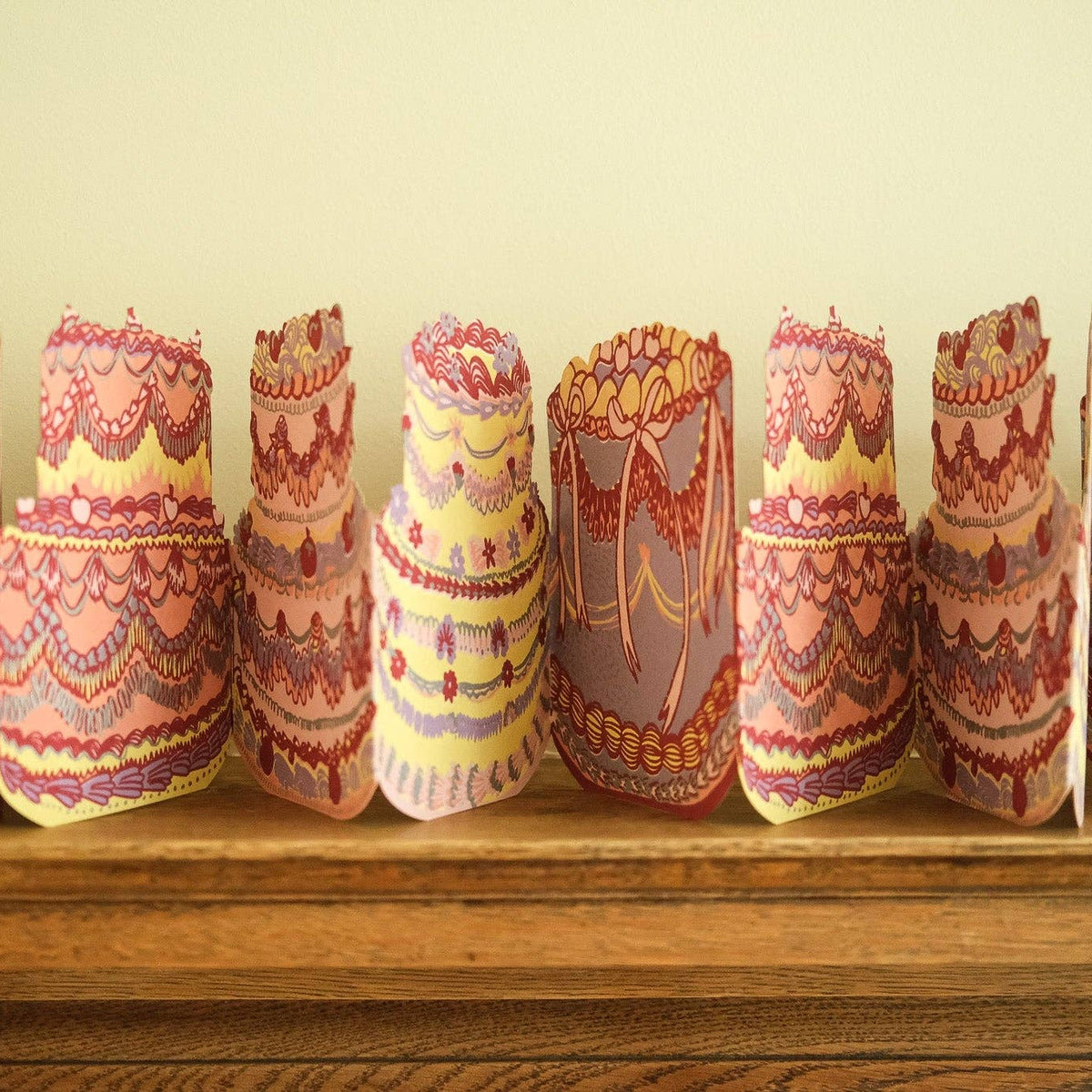 Decorative paper cake models on a wooden surface with a plain background