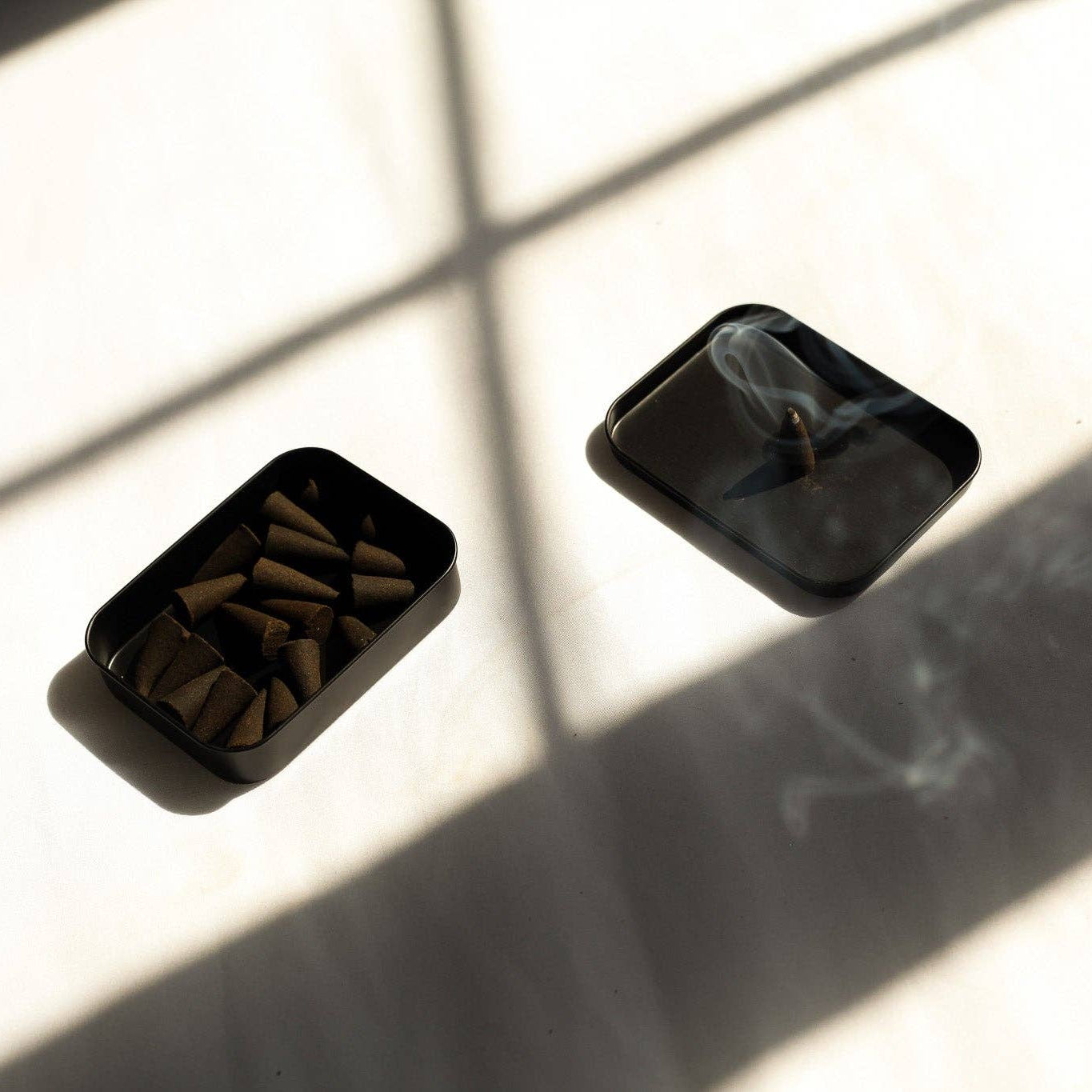 Two black rectangular containers with small items on a light surface with shadows.