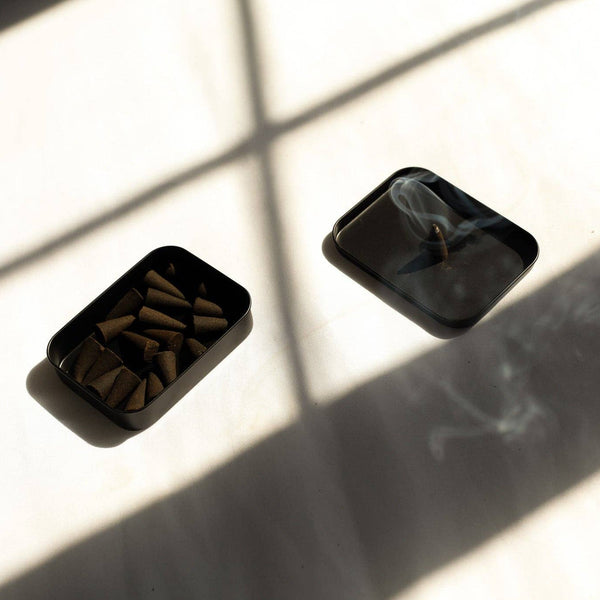 Two black rectangular containers with small items on a light surface with shadows.