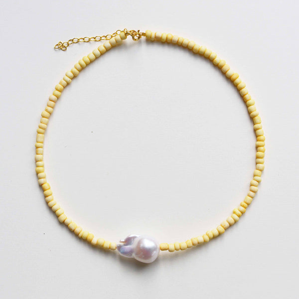 Necklace with yellow beads and a central pearl on a light gray background