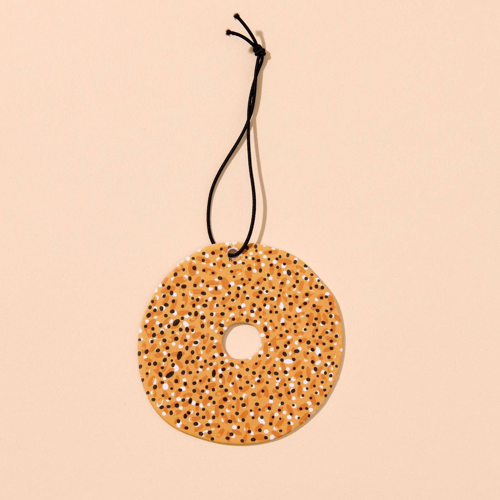 Round decorative air freshener in the shape of an everything bagel, hung on a black string on a beige background