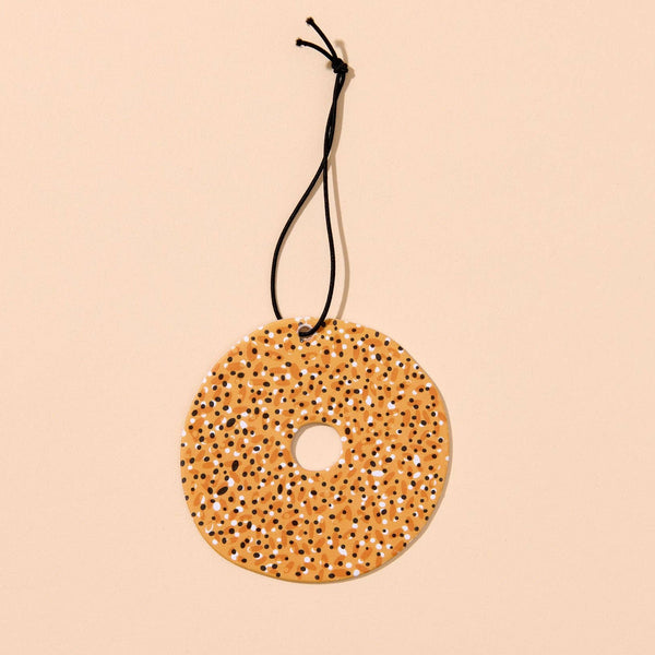 Round decorative air freshener in the shape of an everything bagel, hung on a black string on a beige background