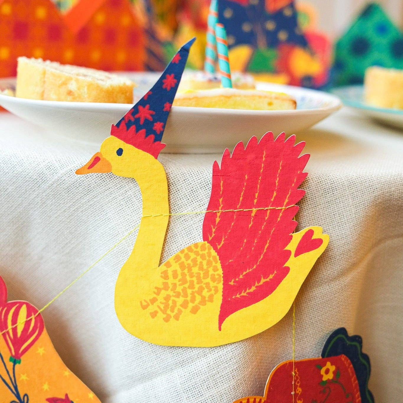 Colorful paper swan decorations on a tablecloth with a blurred festive background.