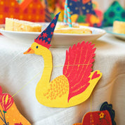 Colorful paper swan decorations on a tablecloth with a blurred festive background.