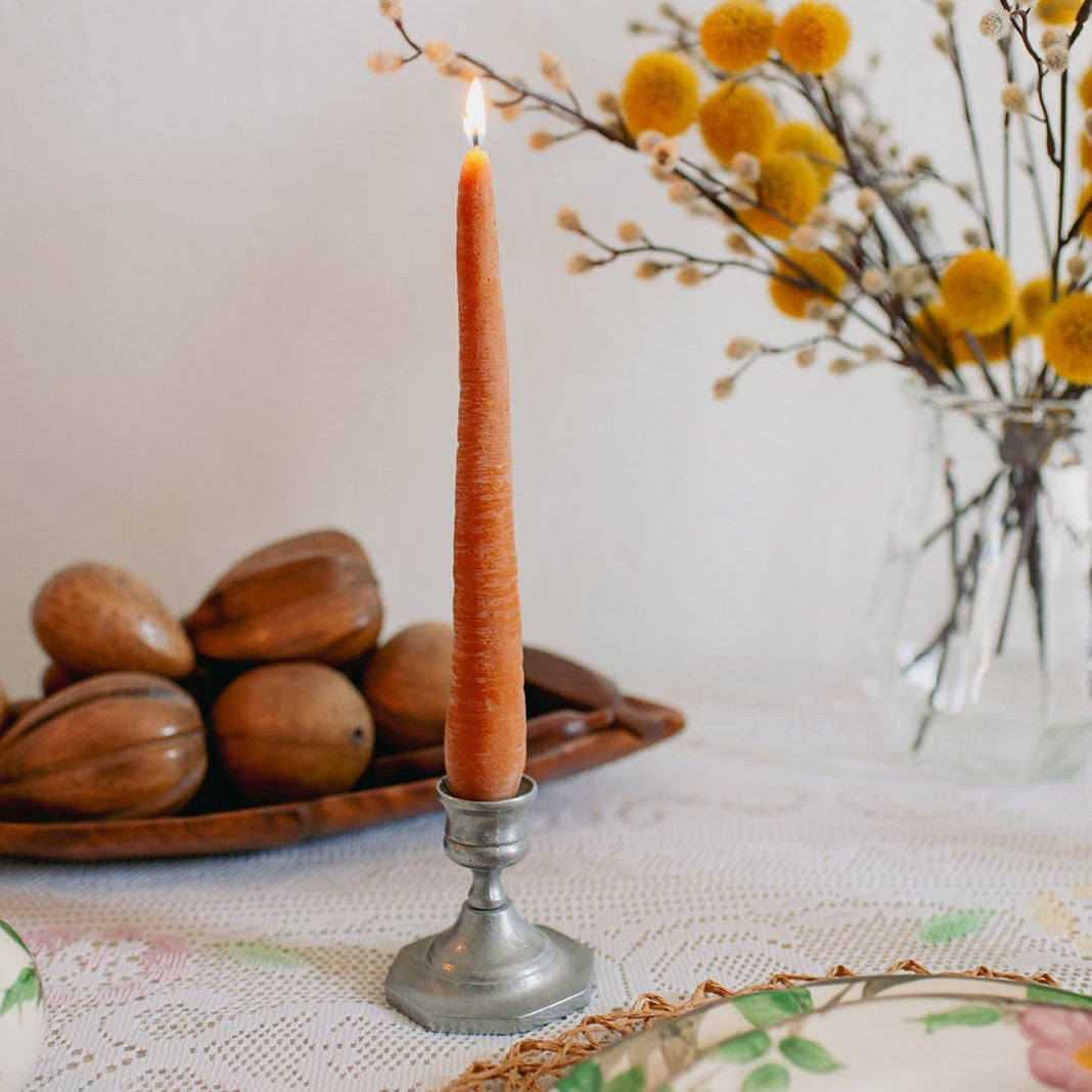 Orange candle in a metal holder on a table with decorative elements.