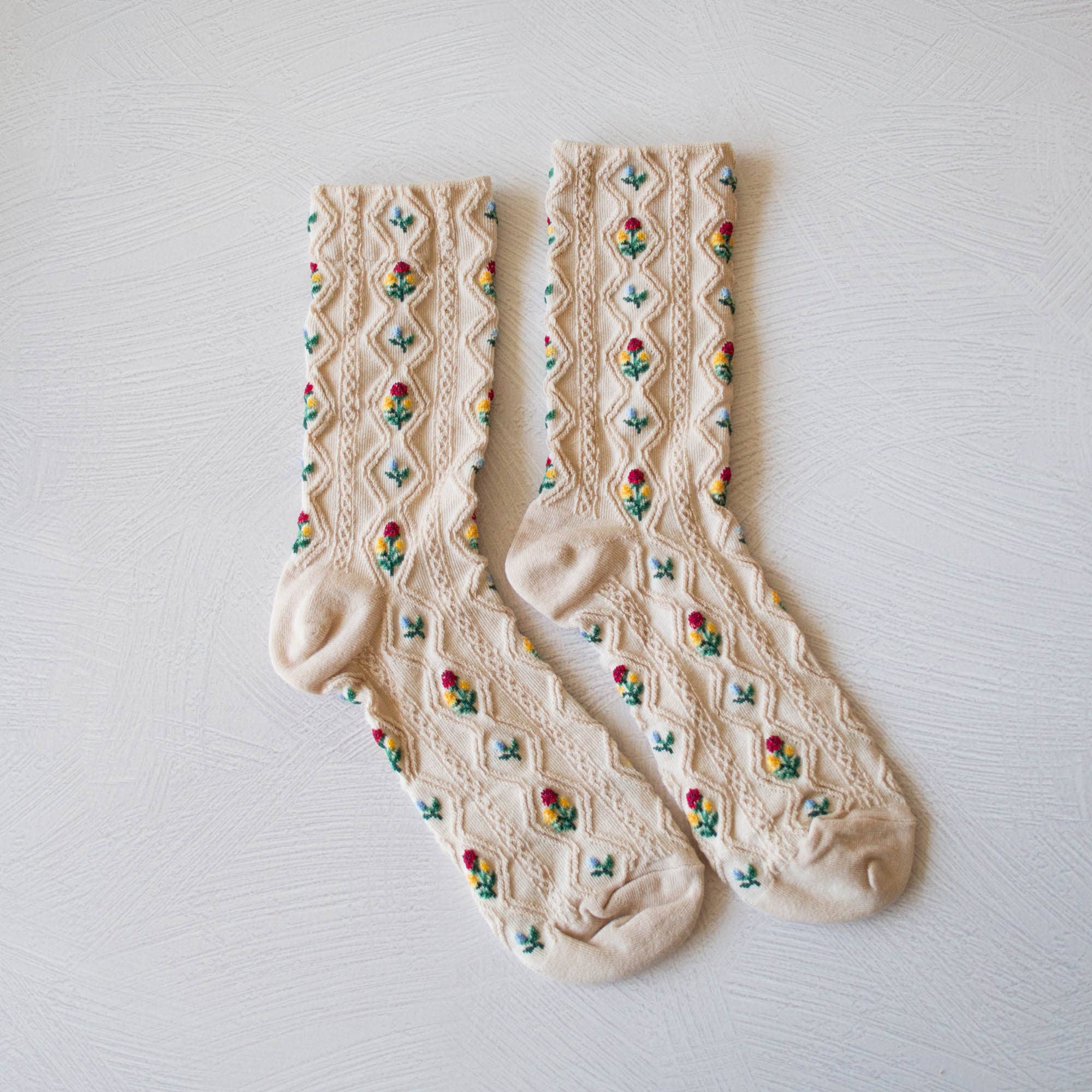 Pair of cream-colored socks with floral patterns on a light gray background
