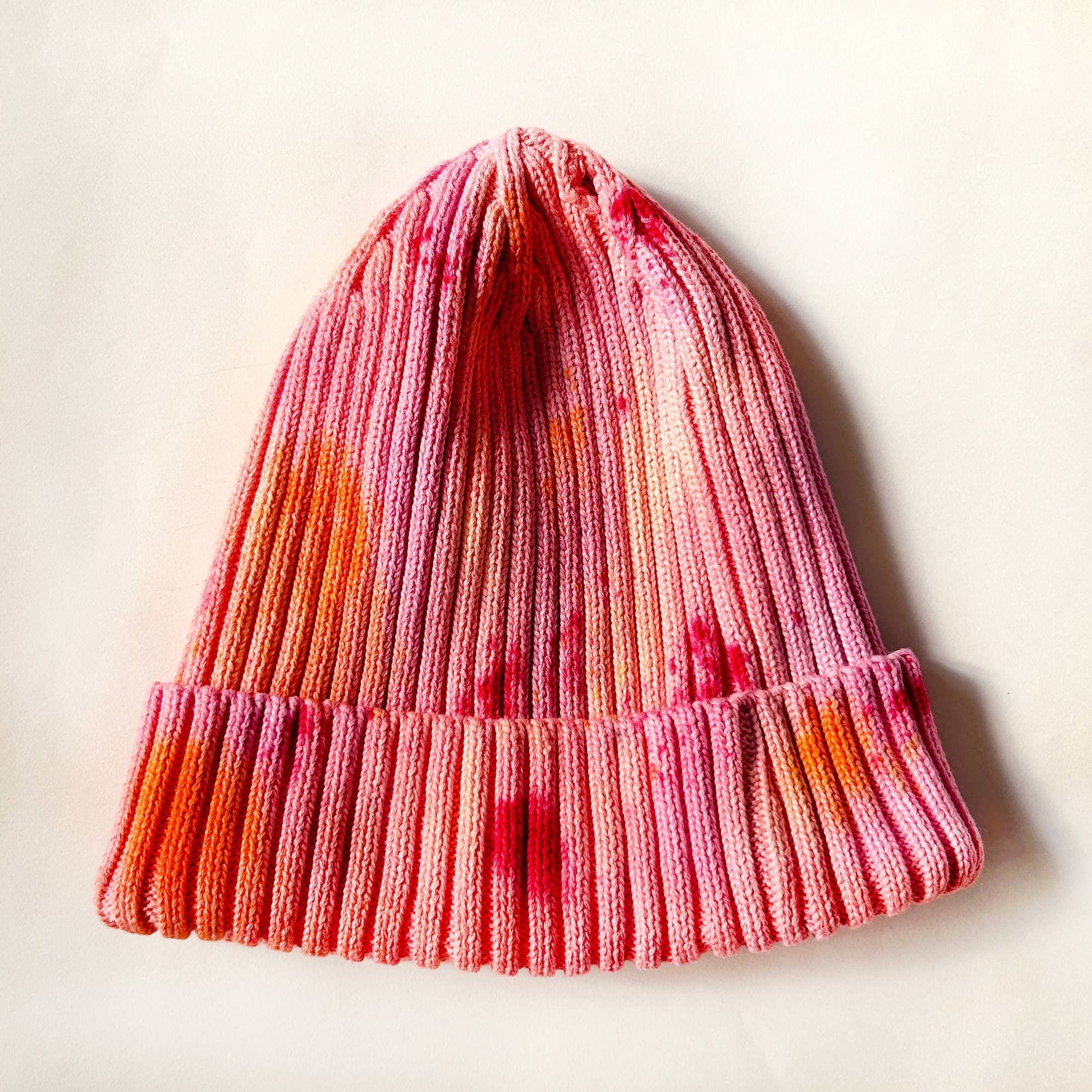 Knitted beanie with a gradient of pink, orange, and red on a light background