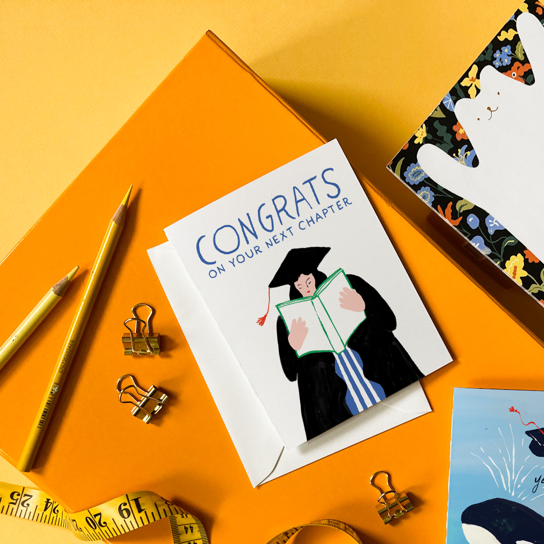 Graduation-themed cards, a box with a cat design, and stationery items on a yellow background