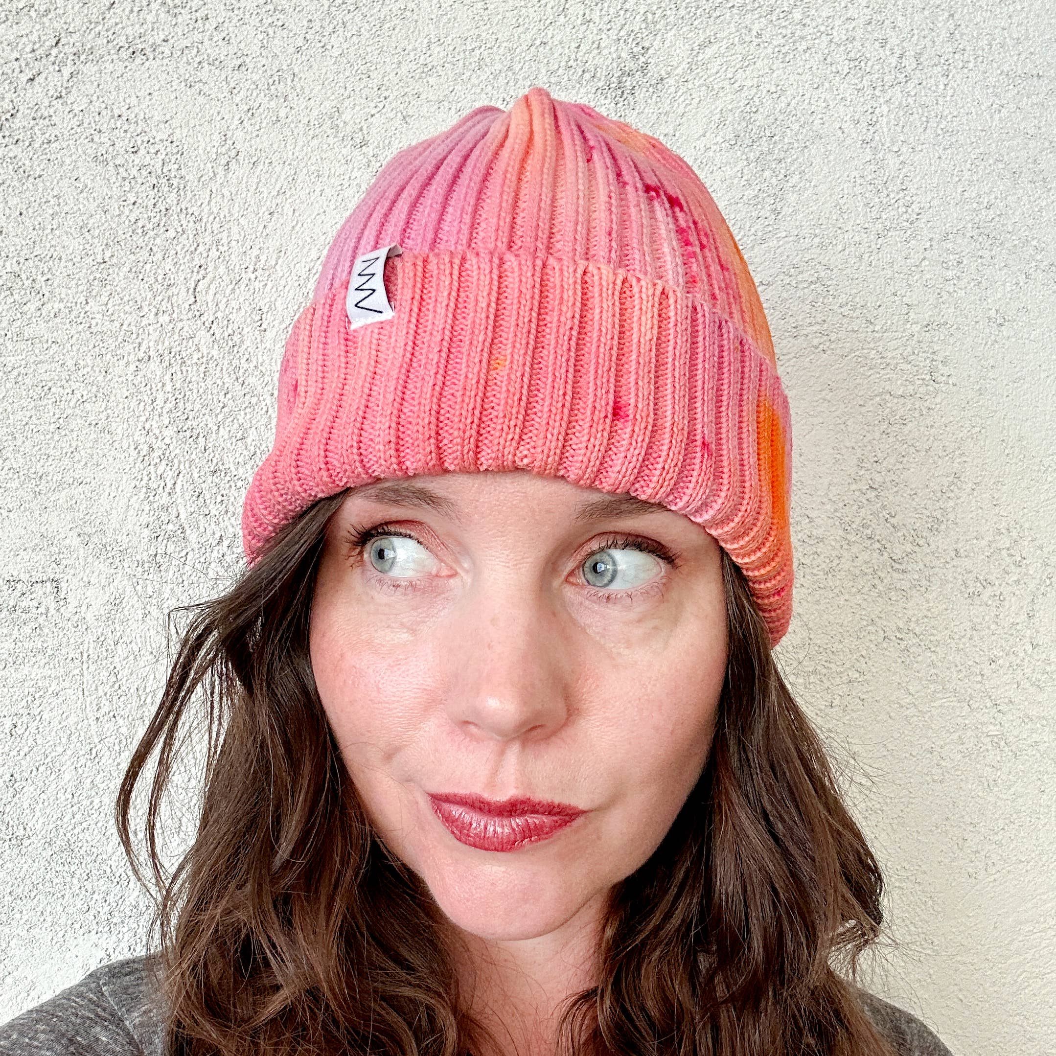 Person wearing a pink and orange beanie with a brand logo against a light background