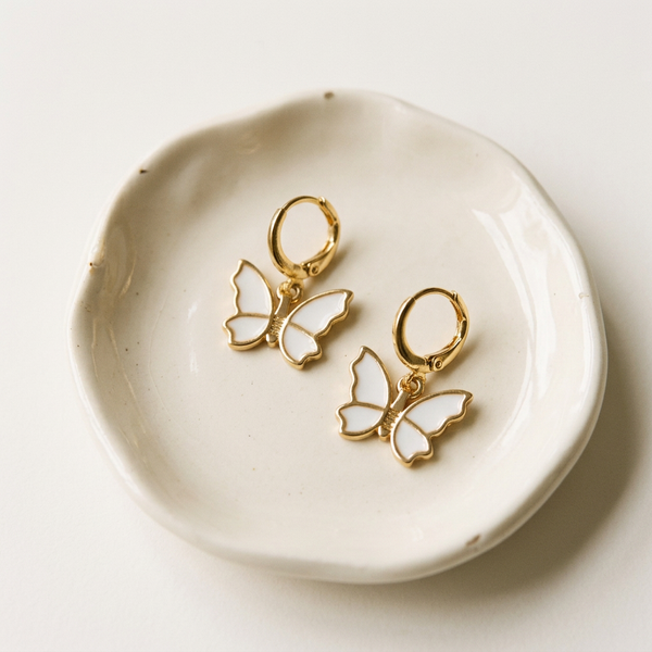 Gold butterfly earrings on a white ceramic dish