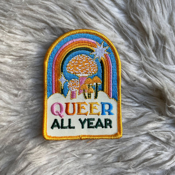 Embroidered patch with rainbow, sun, and 'Queer All Year' text on a fluffy white background