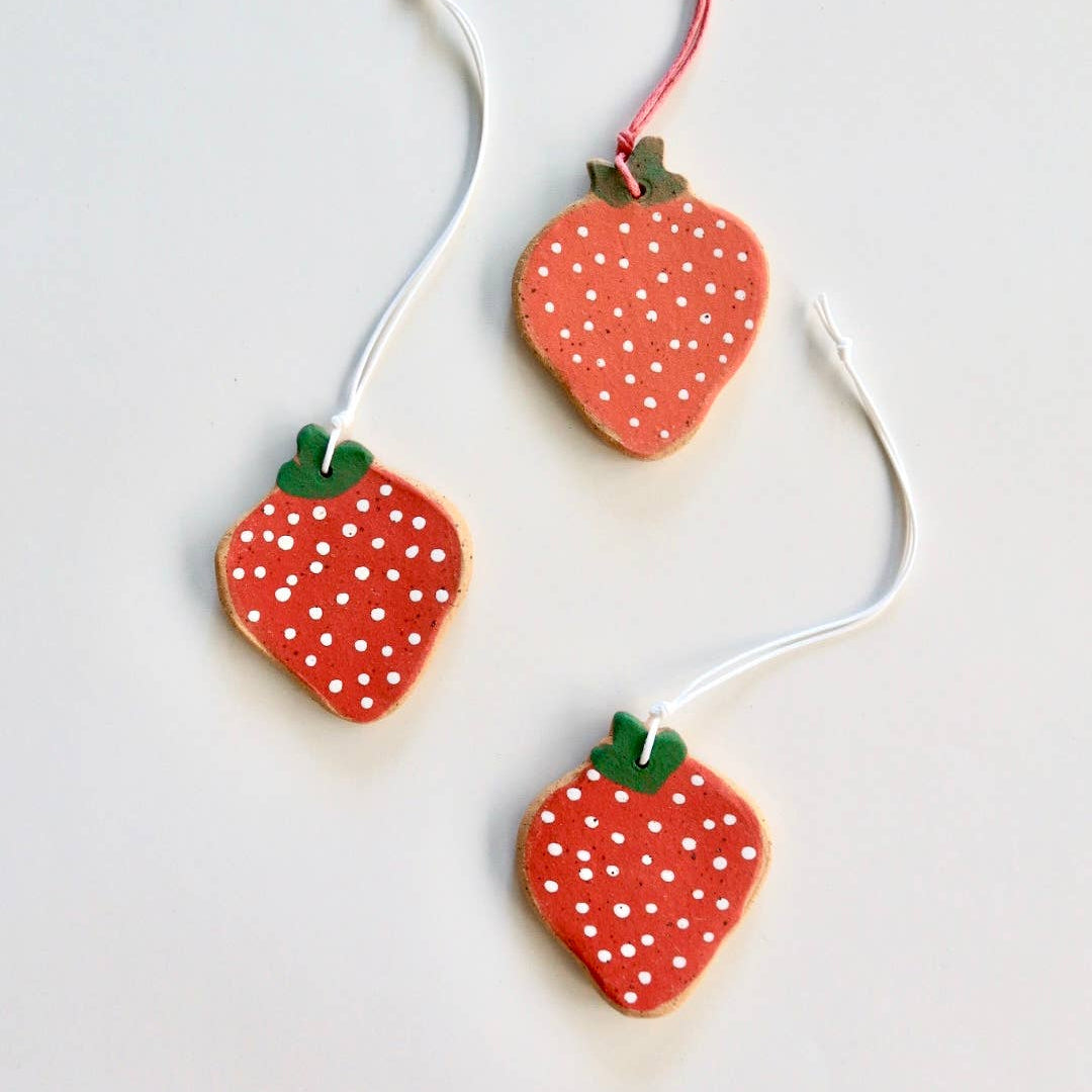 Three ceramic strawberry ornaments with hand painted details, strung with nylon chords.