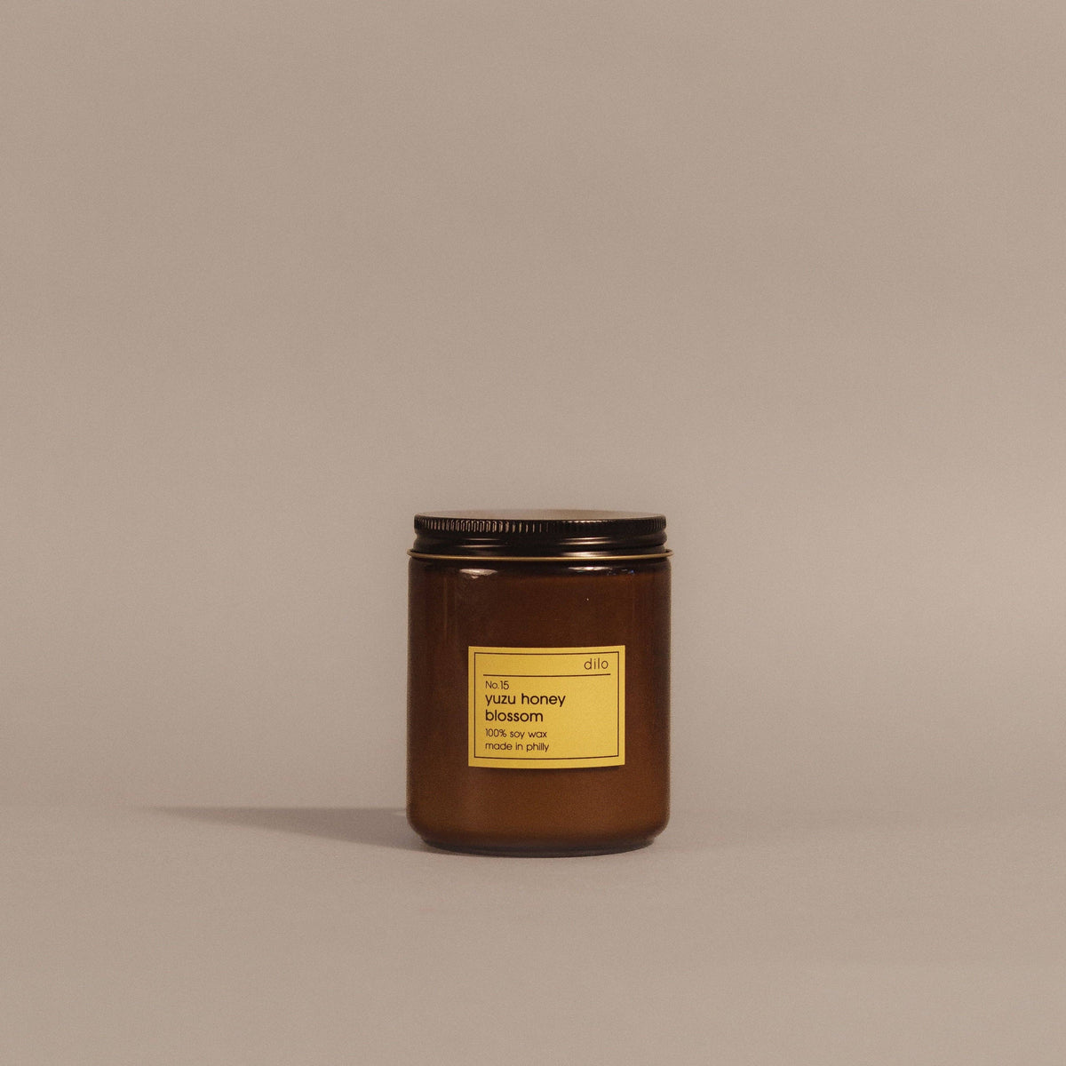 An amber glass jar candle with a black metal lid and a yellow label reading 'dis. beeswax honey blossom 100% beeswax' on a warm taupe background.