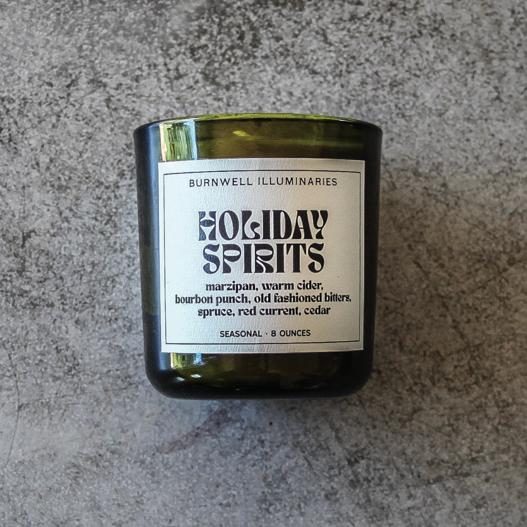 Candle in a bottle labeled 'Holiday Spirits' on a gray surface